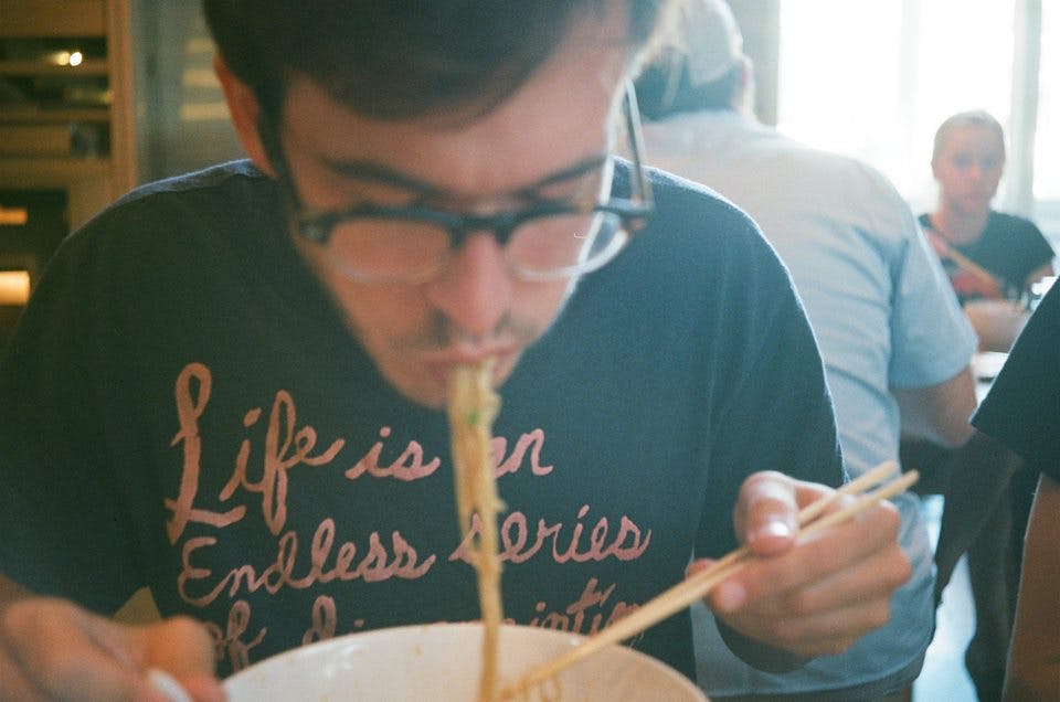 A film photo of myself slurping from a bowl of ramen noodles at Momofuku.